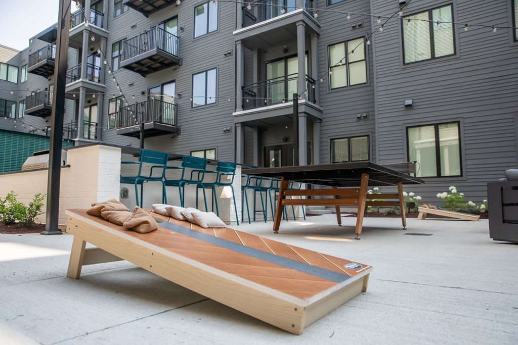 A wooden bench with cushions is in front of a modern apartment building.