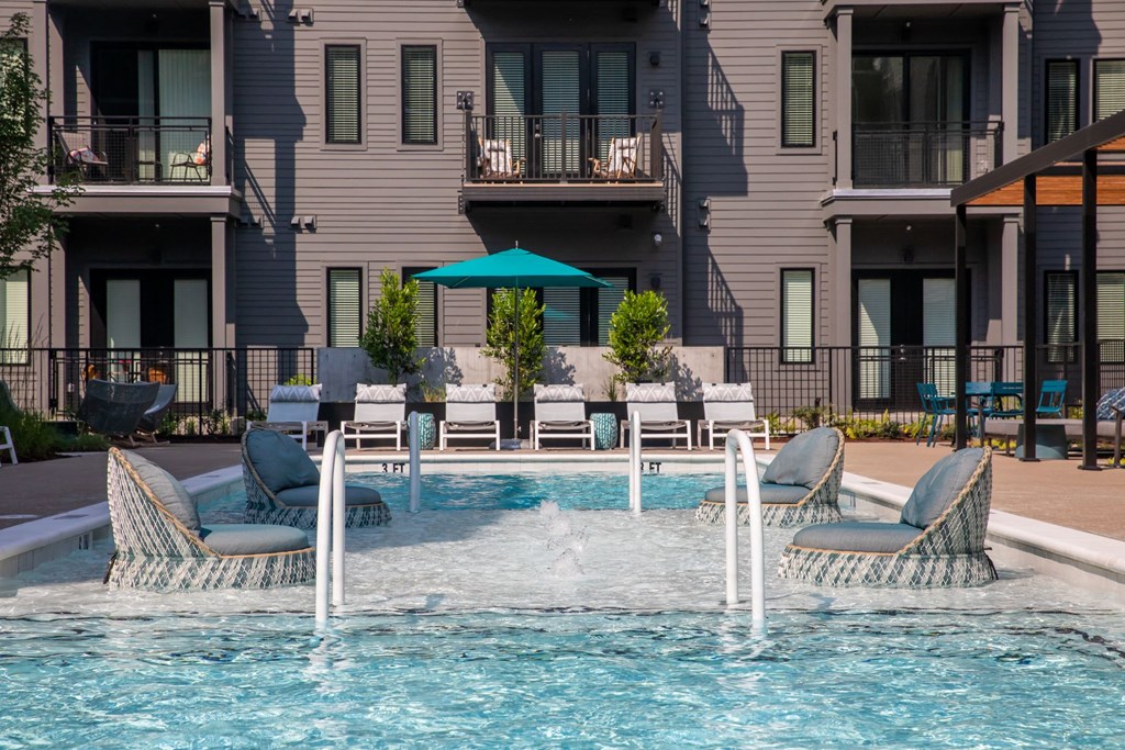 A pool with chairs and umbrellas in front of a building.