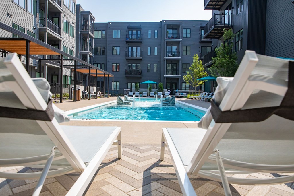 Two white chairs are facing a pool in a courtyard.