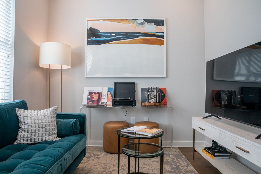 A living room with a green couch, a table with a lamp, a painting on the wall, and a television.