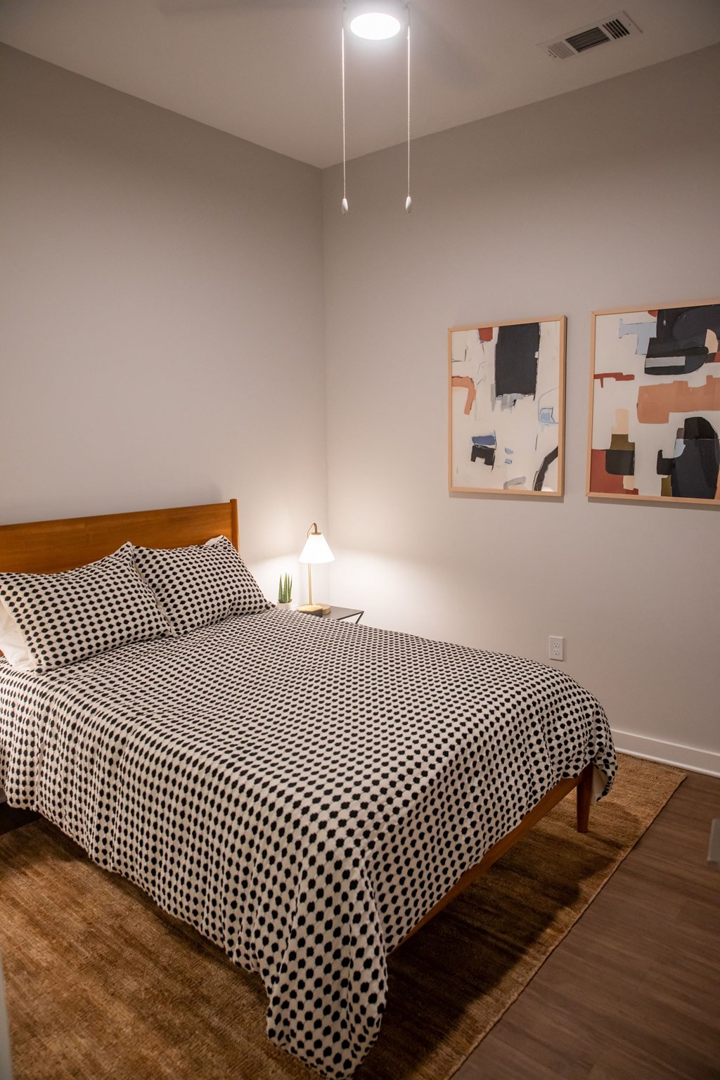 A bed with a black and white comforter sits in a room with two paintings on the wall.