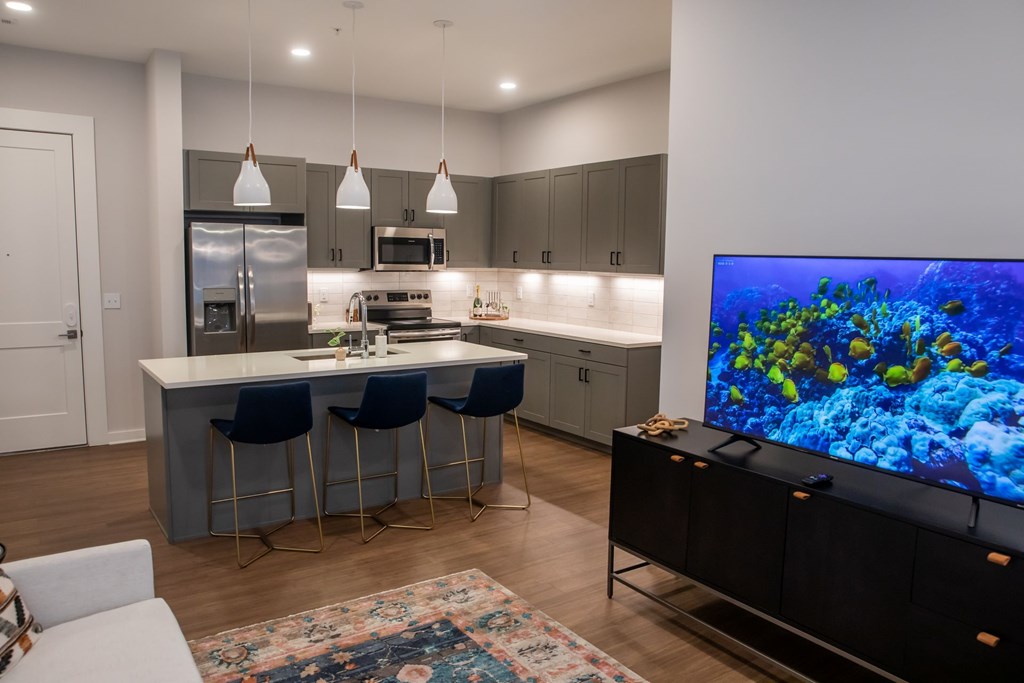 A modern kitchen with a bar area and a television displaying an underwater scene.