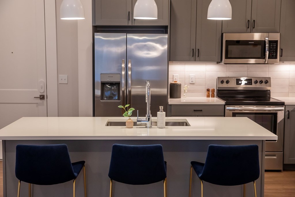 A modern kitchen with a white island and blue chairs.