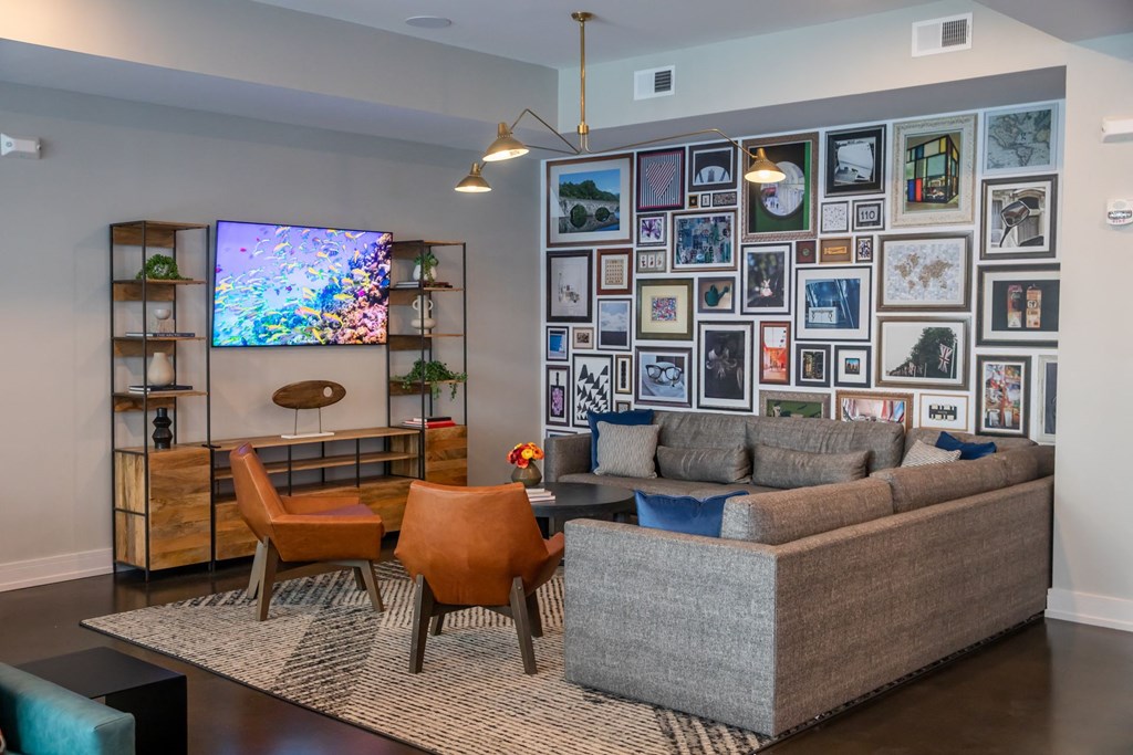 A living room with a grey couch, orange chairs, and a TV on a wooden stand.
