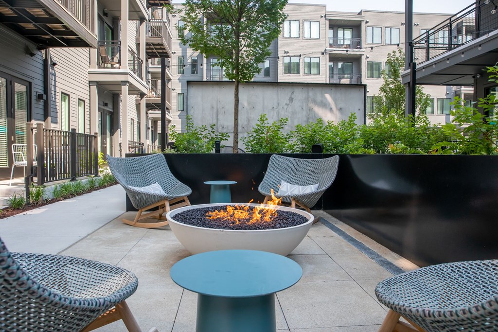 A fire pit sits in the middle of a patio surrounded by chairs.