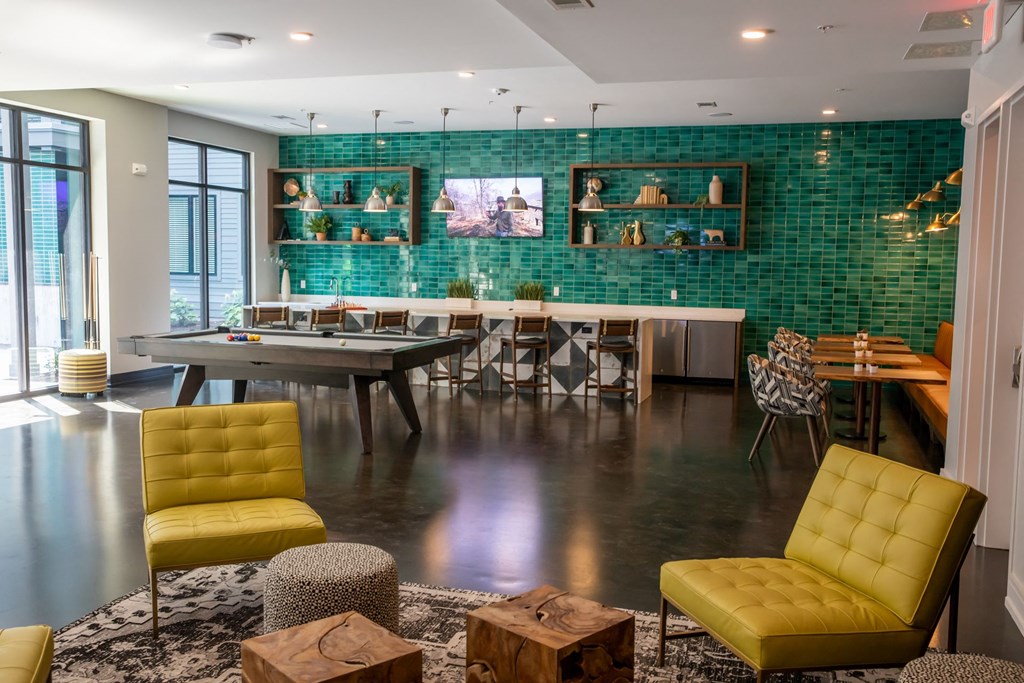 A modern living room with a green tiled wall and yellow chairs.