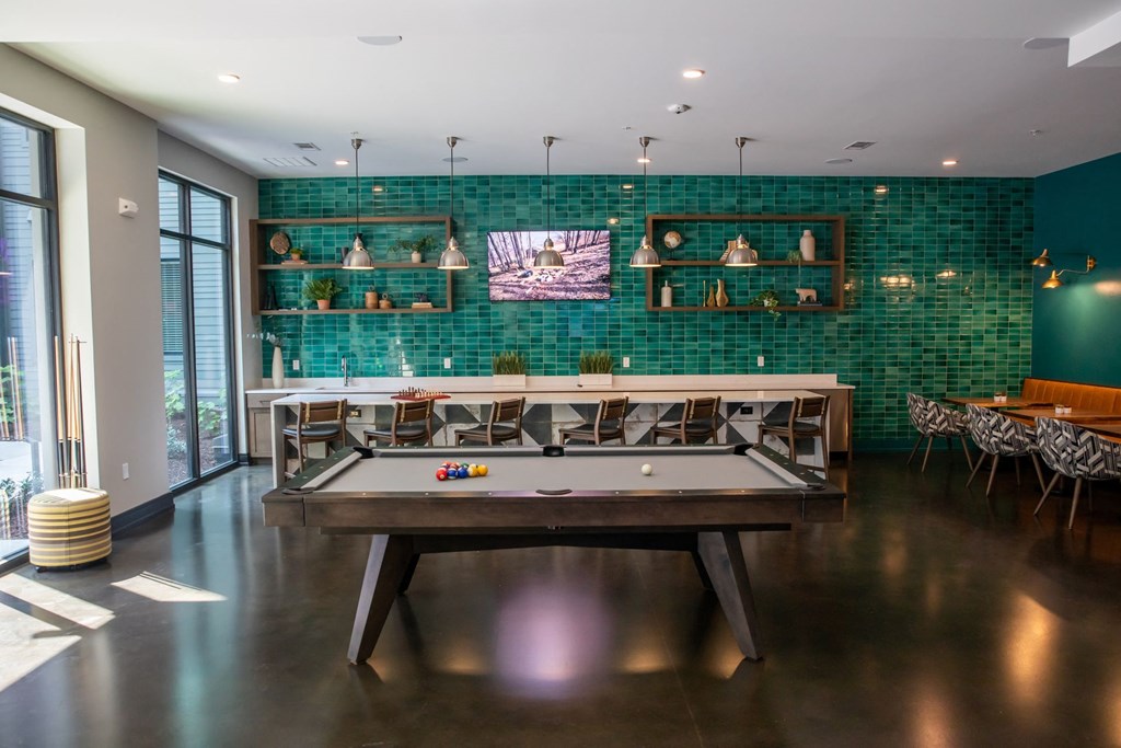 A pool table is in the middle of a room with a green tiled wall.