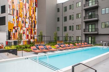 A pool surrounded by orange lounge chairs in front of a building with a mural.