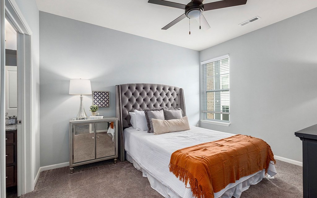 A bedroom with a bed, a ceiling fan, and a nightstand with a lamp.