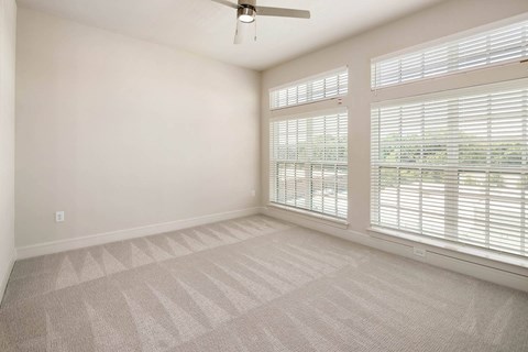 an empty living room with large windows and a ceiling fan