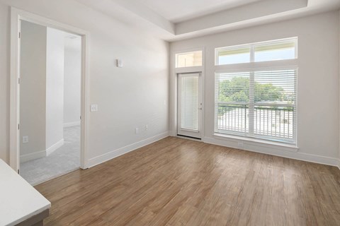 an empty living room with wood floors and a door to a balcony