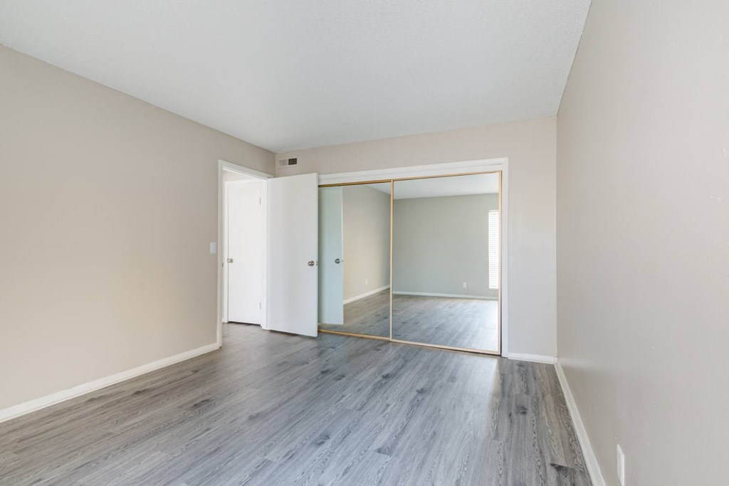 an empty living room with wood floors and a mirrored closet