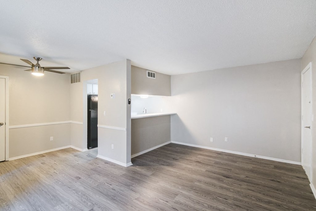 the living room and kitchen of an empty apartment with wood floors and a ceiling fan