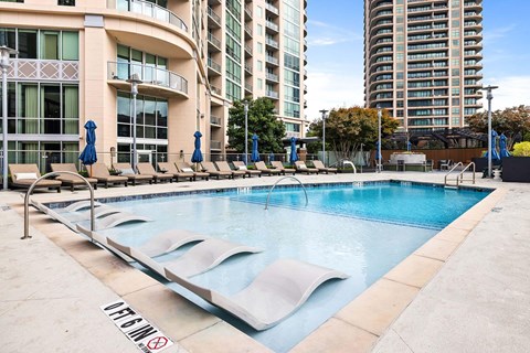 Luxury Apartments in Buckhead, GA, With In-Unit Washer and Dryer - The Huntley - Resort-Style Swimming Pool With In-Water Lounge Chairs, Sundeck Seating, Blue Umbrellas, and High-Rise Views.