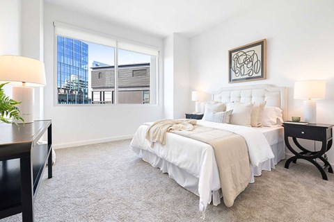 Dog-Friendly Luxury Apartments in Buckhead, GA - The Huntley - Spacious Bedroom With Plush Carpet, White Bedding, Large Window, Nightstands, Lamp, and Wall Art.