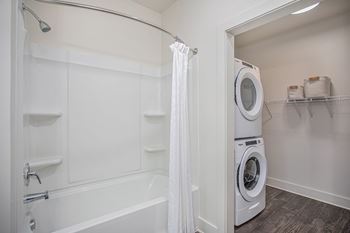 A white bathroom with a tub and a washer and dryer.