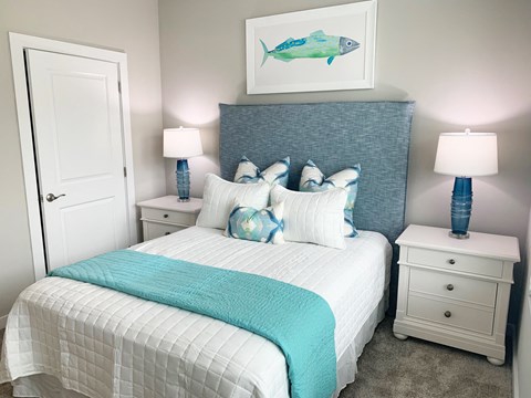 One-Bedroom Apartments in Pensacola, FL - Preserve at Perdido - Bedroom with a Textured Headboard-Bed Flanked by Two Nightstands with Lamps Set off with a Carpet, Oceanic Decor, and Neutral Walls.