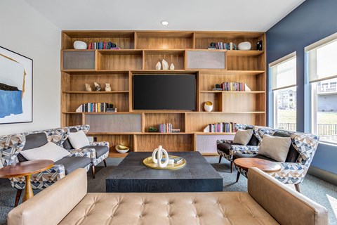 A living room with a brown leather sofa, a coffee table, and a bookshelf with a flat screen TV on top.