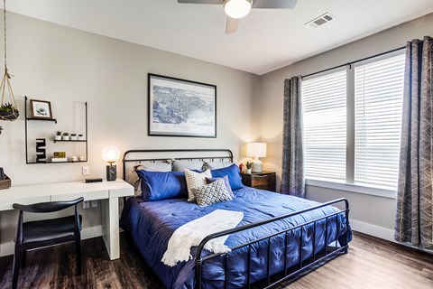 A bedroom with a blue bed and a white desk.