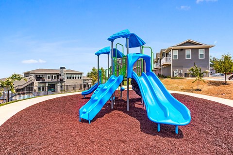 A blue playground slide in the foreground with a residential building in the background.