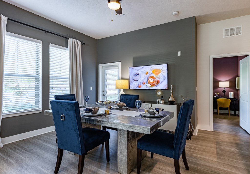 Dog-Friendly Apartments in Altamonte Springs, FL - Nine12 Gateway - Dining Area with Vinyl Plank Flooring, Dining Table, Chairs, Storage Cabinet, Wall-Mounted TV, Ceiling Fan, and Large Windows.