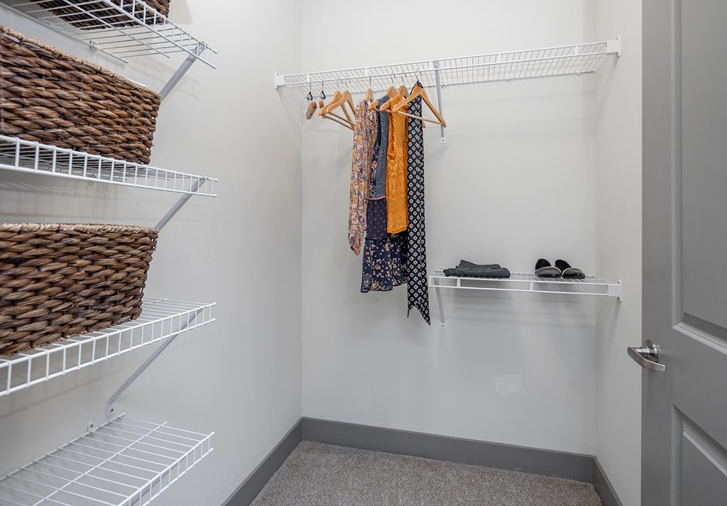 a walk in closet with white walls and shelves and a closet door open with clothes
