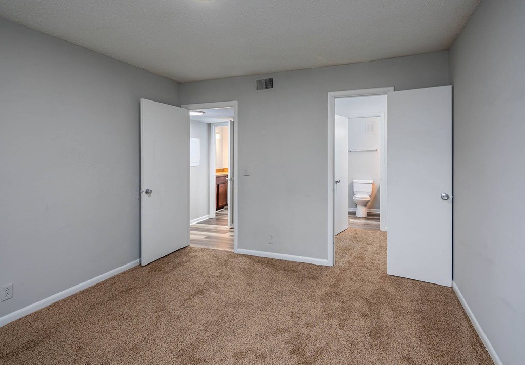 a bedroom with two doors and a bathroom in the background