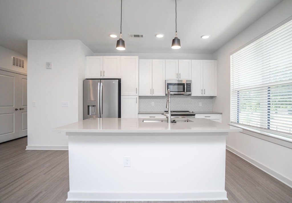 a white kitchen with a large island and a stainless steel refrigerator