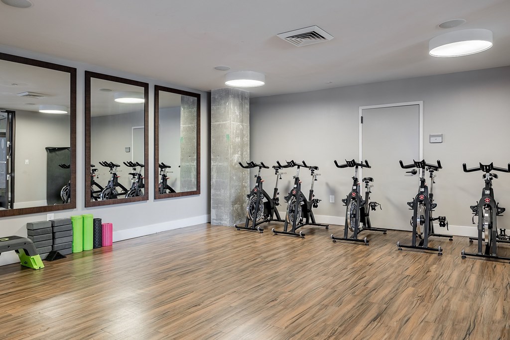 A room with a row of stationary bikes and a mirror on the wall.