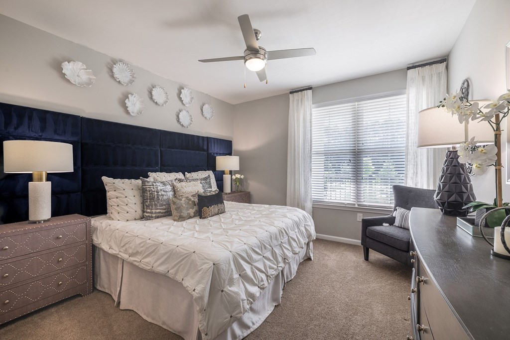 A bedroom with a bed, a dresser, a chair, and a ceiling fan.