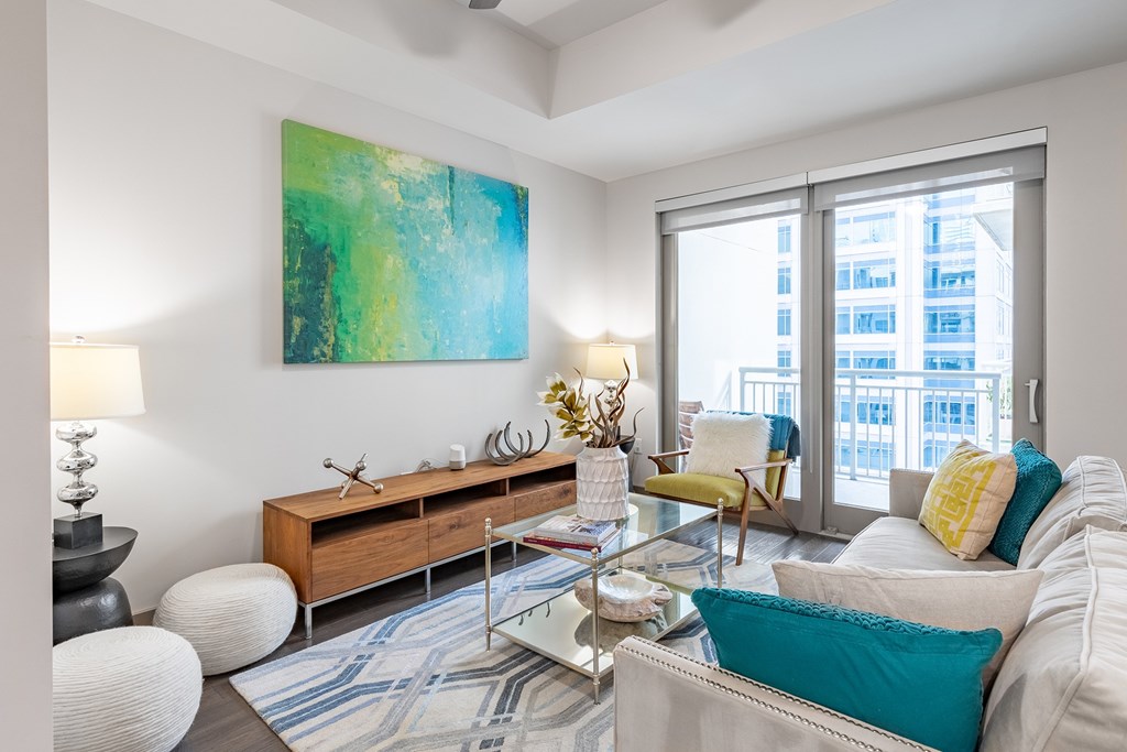 A living room with a large painting on the wall and a view of a cityscape through the windows.