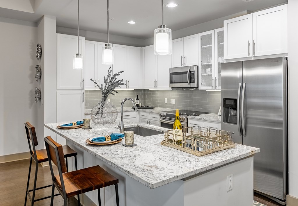 Luxury Apartments in Midtown Atlanta, GA with In-Unit Washer and Dryer  - Trace Midtown - Kitchen With White Cabinetry, Stainless Steel Appliances, Granite Countertops, Tile Backsplash, and Island with Pendant Lights and Bar Seating.