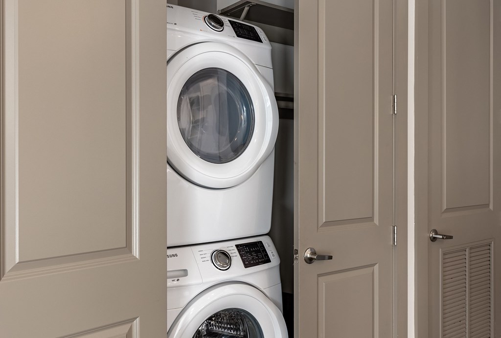 A white washing machine is stacked on top of another white washing machine in a cabinet.