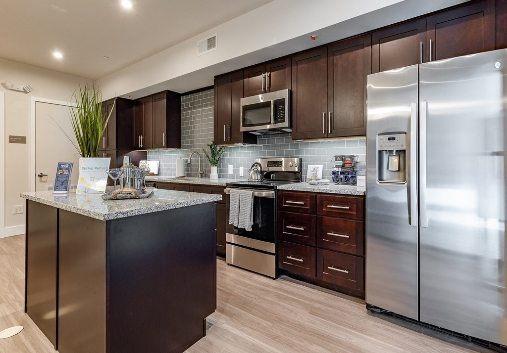 Pet-Friendly Apartments in Altamonte Springs, FL - Nine12 Gateway - Kitchen with Vinyl Plank Flooring, Island, Quartz Countertops, Stainless Steel Appliances, and Dark Brown Cabinetry.