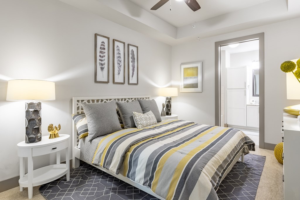 Midtown Atlanta, GA Luxury Apartments with In-Unit Washer and Dryer - Trace Midtown - Bedroom with Carpet Flooring, Area Rug, Large Bed, Nightstands with Lamps, Dresser, Ceiling Fan, and Attached Bathroom.