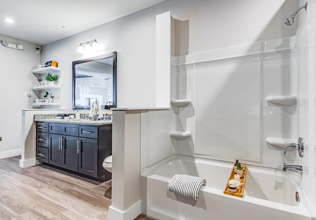 1-Bedroom Luxury Apartments in Altamonte Springs, FL - Nine12 Gateway - Bathroom with Vinyl Plank Flooring, Garden Tub Shower, Large Sink Vanity, and Floating Shelves.