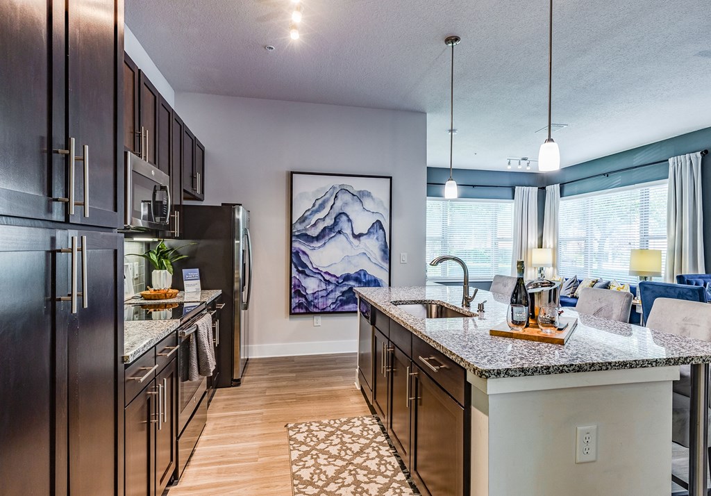 Luxury Apartments for Rent in Altamonte Springs, FL - Nine12 Gateway - Modern Kitchen with Wood-Style Vinyl Plank Flooring, Dark Wood Cabinetry, Large Cooking Island with Sink and Bar Chairs, Pendant Lights, Granite Countertops, and Stainless Steel Appliances