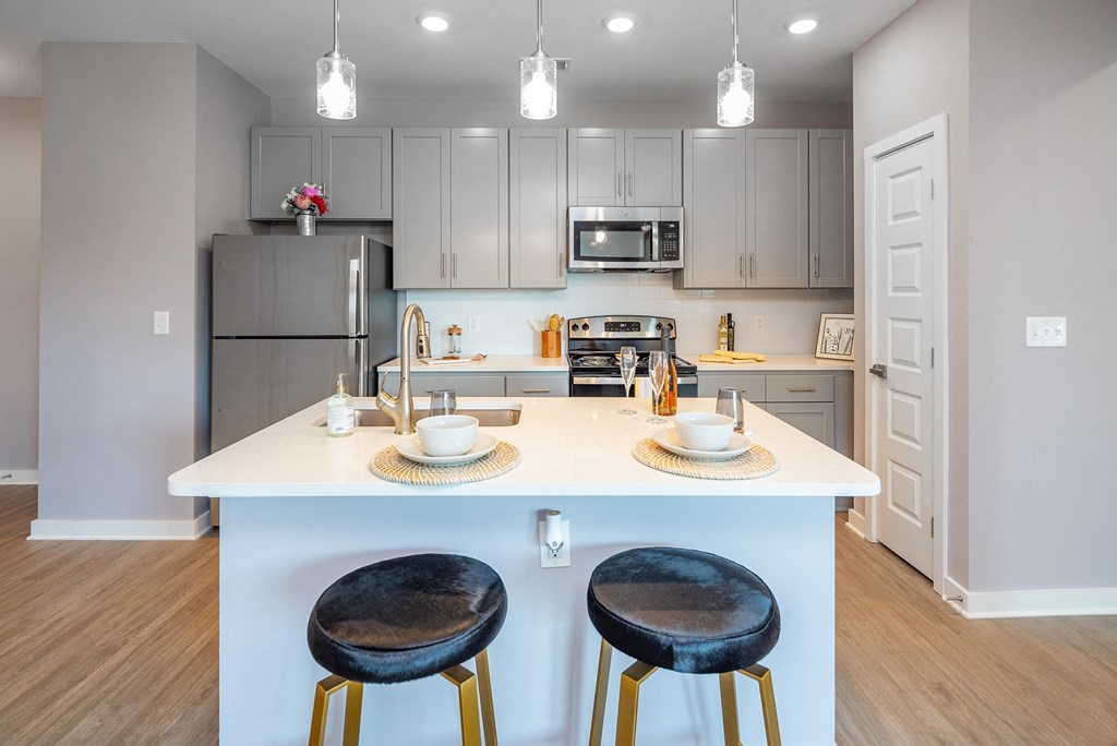 1-Bedroom Apartments in Mt. Juliet, TN - The Enclave at Providence - Kitchen with Hardwood-Style Flooring, Island with Seating, Pendant Lights, Granite Countertops, Stainless Steel Appliances, and Grey Shaker-Style Cabinets.
