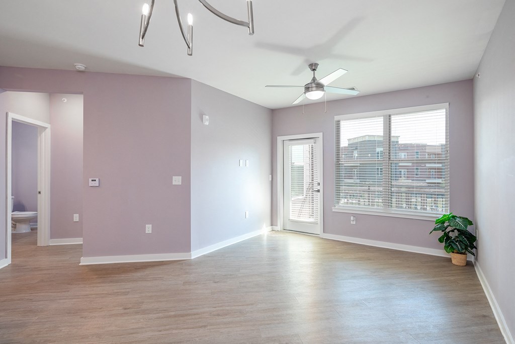 Mt. Juliet Apartments for Rent - The Enclave - Empty Living Room with Hardwood-Style Flooring, Pink Walls, Ceiling Fan, Window with Blinds, and Door with Access to Balcony/Patio