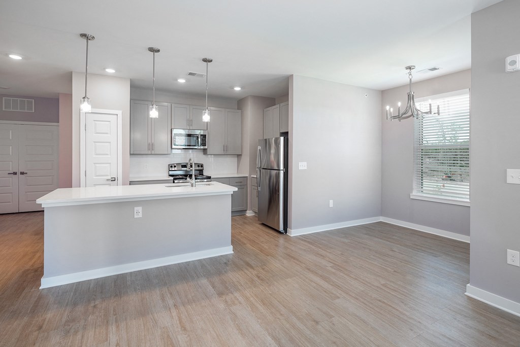 an open kitchen and living room with a white island and a stainless steel refrigerator