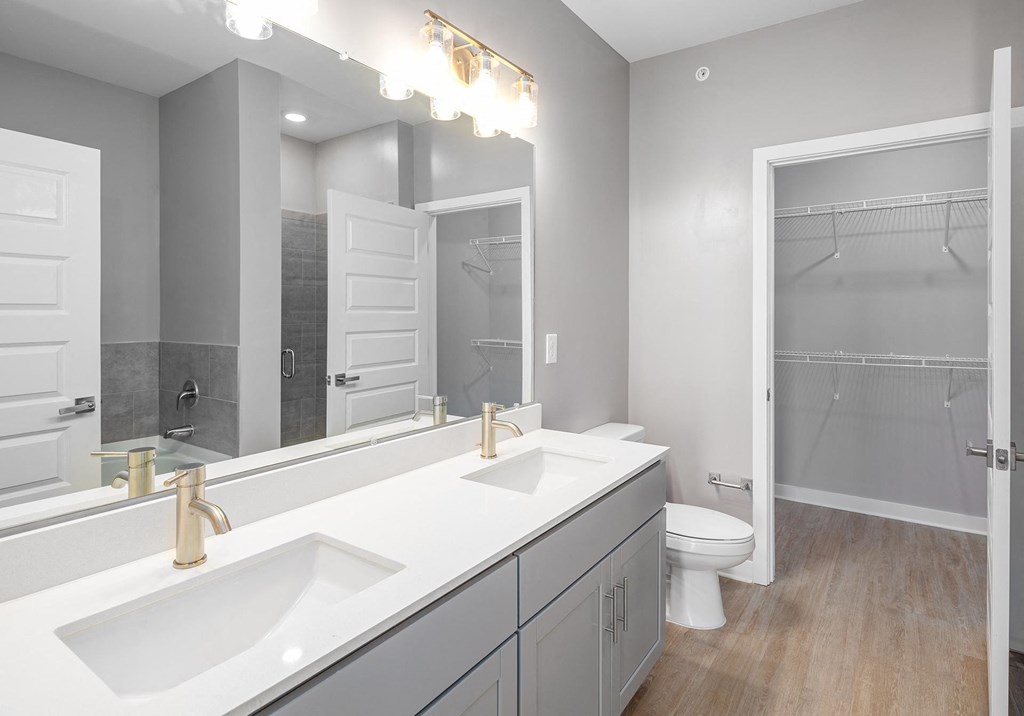 Mt. Juliet TN Apartments - The Enclave - Bathroom with Hardwood-Style Flooring, Double Sinks, Granite Countertop, Large Vanity Mirror, and Spacious Walk-In Closet with Storage Shelves