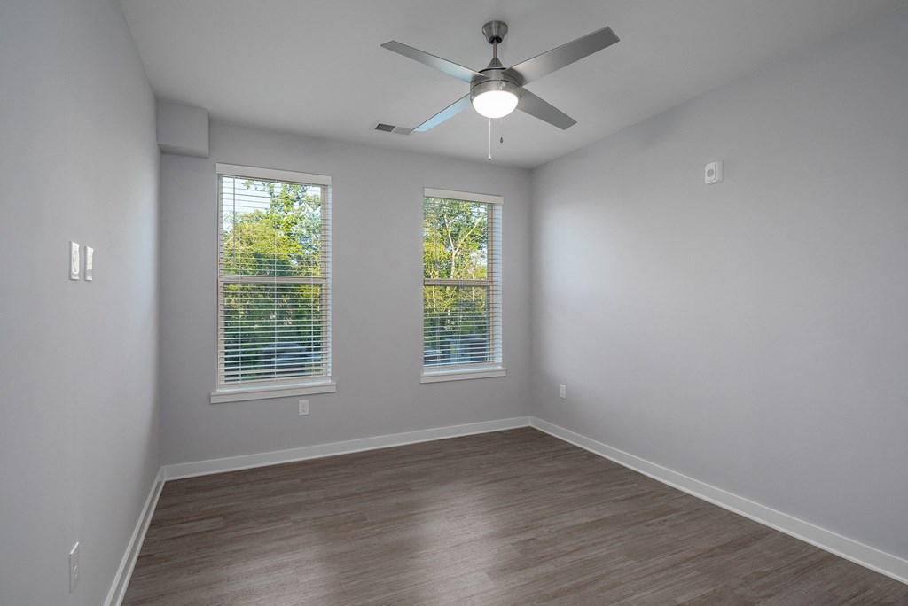 an empty room with a ceiling fan and two windows
