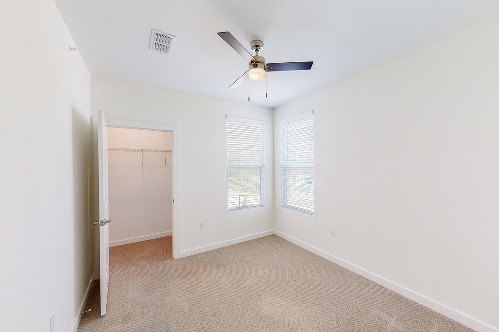 an empty room with a ceiling fan and two windows