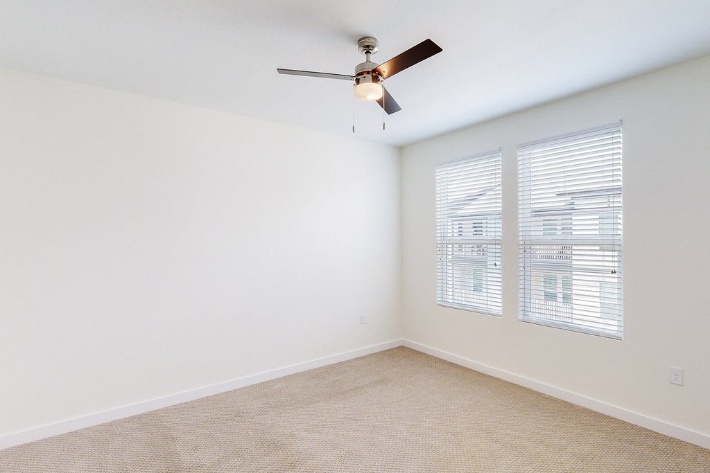 an empty room with a ceiling fan and two windows