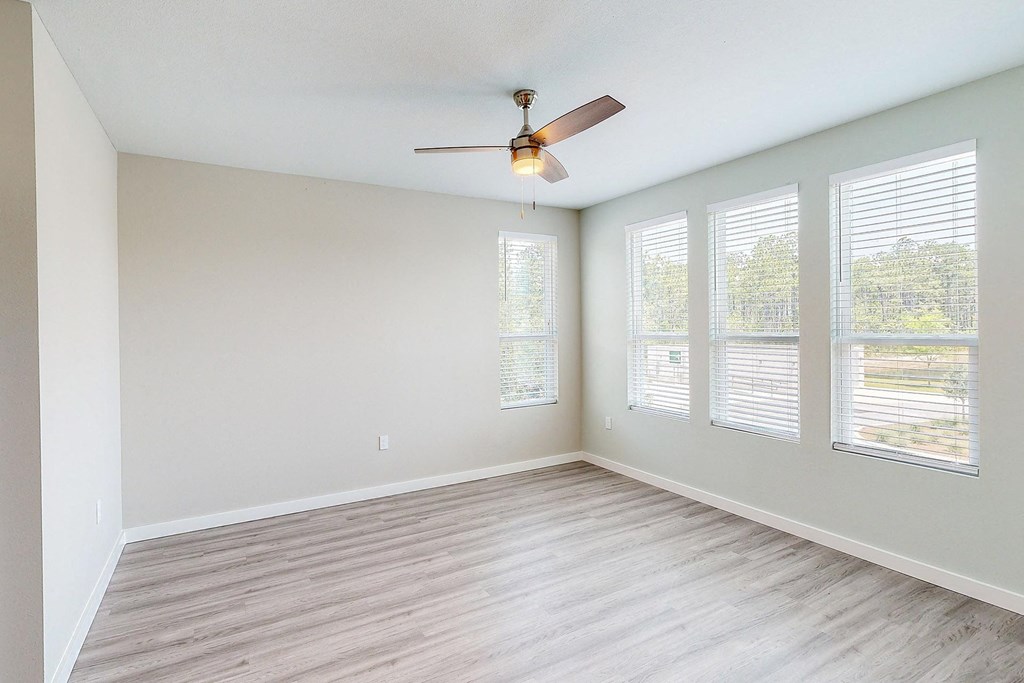 an empty living room with a ceiling fan and windows