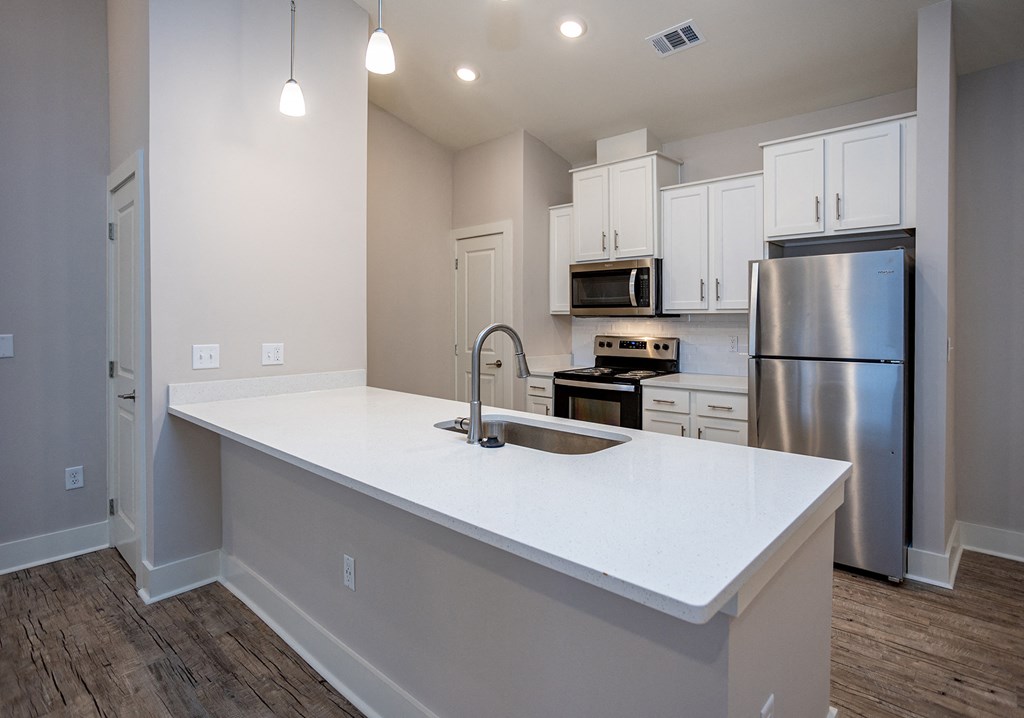 an empty kitchen with a white counter top and a stainless steel refrigerator