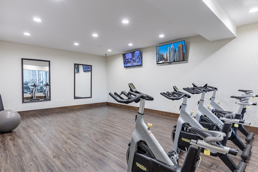 A room with a row of stationary bikes and a TV on the wall.