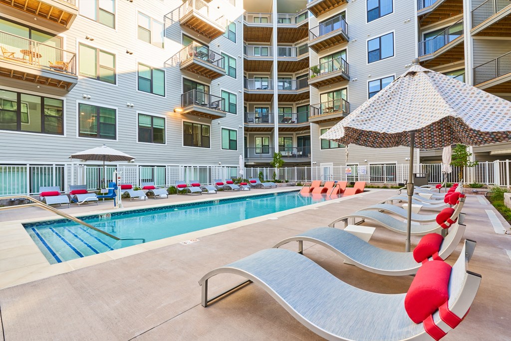 a swimming pool with chairs and an umbrella in front of an apartment building