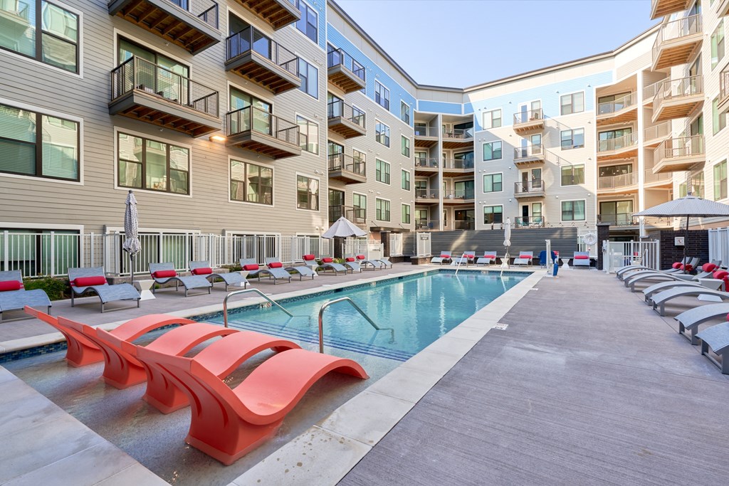 a swimming pool with red lounge chairs in an apartment building
