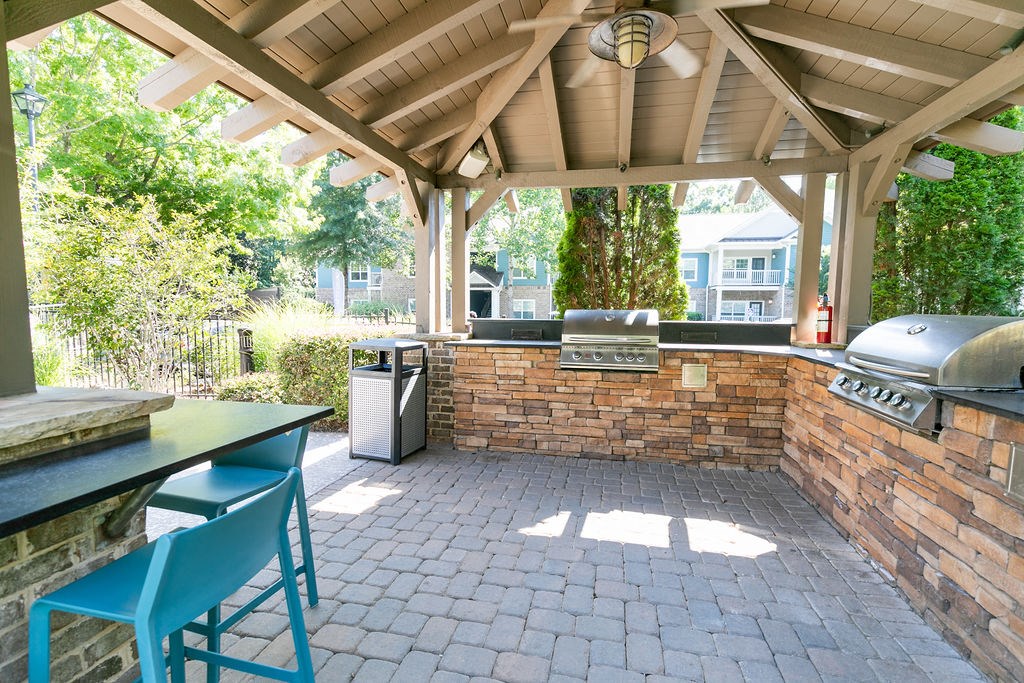Apartments for Rent in Newnan, GA - The Jackson - A Grilling Station Featuring a Covered Kitchen with a Bar Table and Chairs, Ceiling Fan, and Stainless Steel Grills.